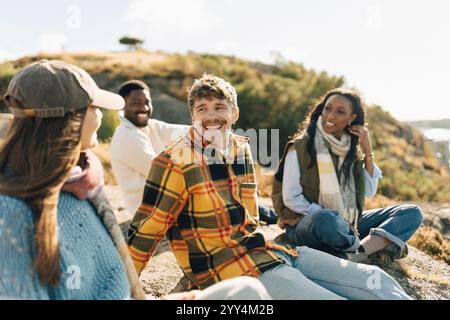 Happy young man talking with female friend while sitting on hill at sunny day Stock Photo