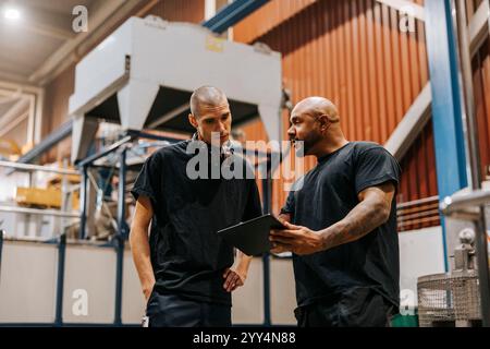 Low angle view of mature man holding tablet PC while discussing with male colleague in manufacturing factory Stock Photo
