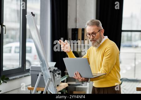 Senior man engaged in a work presentation, utilizing a laptop while standing by an easel. Stock Photo