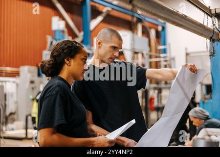 Mature man holding blueprint while standing next to female colleague in warehouse Stock Photo