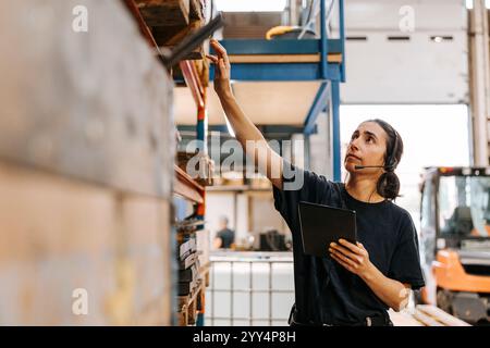 Female worker wearing headset while taking inventory in distribution warehouse Stock Photo