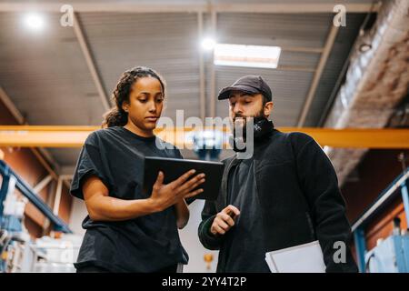 Low angle view of multiracial male and female warehouse workers discussing over tablet PC while standing in factory Stock Photo