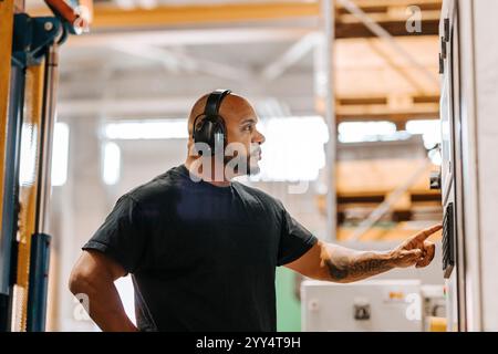 Side view of focused male worker wearing wireless headphones while operating machine in factory Stock Photo