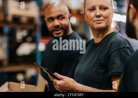 Smiling female worker holding tablet PC while talking with male colleague in warehouse Stock Photo