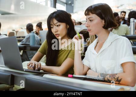 Female university student sitting with young woman using laptop in lecture hall at college Stock Photo