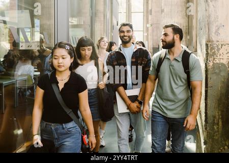 Smiling university student walking with male and female friends at college corridor Stock Photo