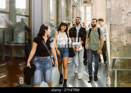 Happy multiracial female and male university students walking in college corridor Stock Photo