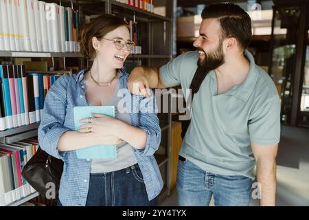 Happy man standing with hand on shoulder of male friend near bookshelf in college library Stock Photo