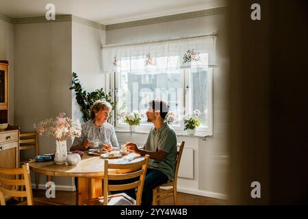 Young male nurse having breakfast with senior woman while sitting at dining table in kitchen Stock Photo