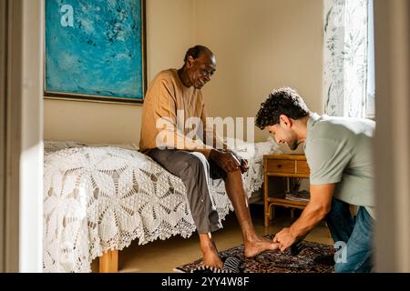 Male nurse helping senior man in wearing sock at home Stock Photo