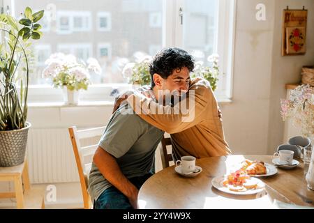 Smiling male nurse embracing senior man sitting at dining table Stock Photo