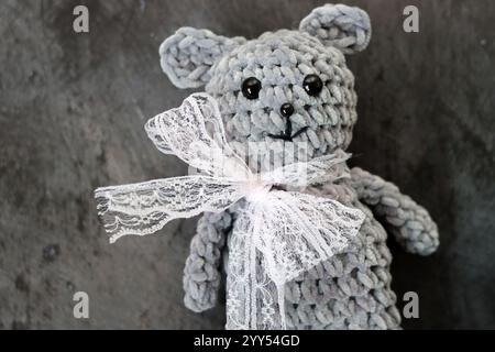 Handmade crochet teddy bear with a bow on a gray background Stock Photo