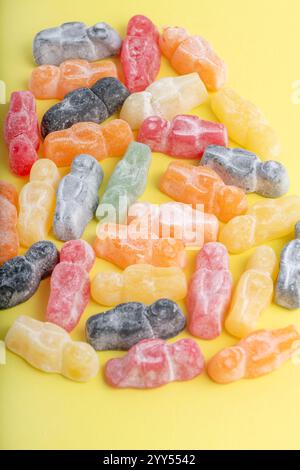 vibrant assortment of multicolored jelly babies arranged on a bright yellow surface. The candies, coated in a fine sugary dust, showcase an array of h Stock Photo