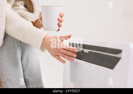 Woman warming hands near electric heater at home. Using heater at home in winter. Woman warming her hands. home heating concept, low temperature Stock Photo