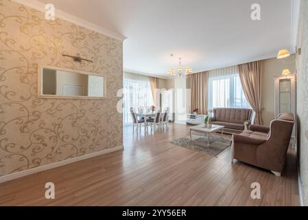 Spacious and bright living room featuring elegant beige and brown decor, classic furnishings, vibrant natural light streaming through large windows. E Stock Photo