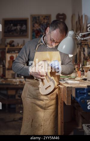 Italian violin maker wearing an apron and gloves is working on a new violin in his workshop, using tools and precision, with a focused expression Stock Photo