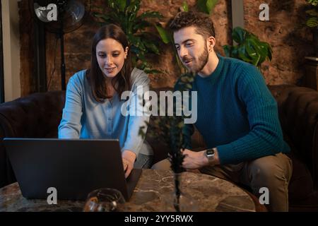 Young adults collaborating on a laptop in a relaxed indoor workspace with natural decorations. Perfect for concepts of teamwork, coworking, learning, Stock Photo