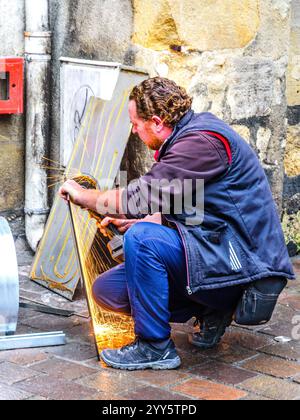 Worker withour safety goggles or face mask using an angle-grinder to cut a metal sheet - Tours, Indre-et-Loire (37), France. Stock Photo