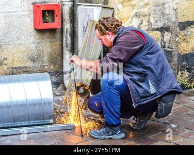 Worker withour safety goggles or face mask using an angle-grinder to cut a metal sheet - Tours, Indre-et-Loire (37), France. Stock Photo