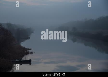 Fisherman boat in river on an early foggy morning at dawn. Dramatic landscapes. Stock Photo