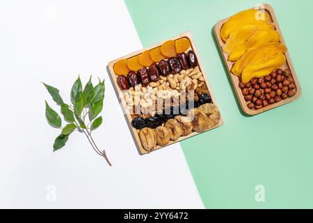 two wooden trays with an assortment of dried fruits and nuts on a white green background with the lights of a young green tree. top view. Flat lay Stock Photo