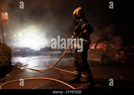 Firefighter trying to put down fire on burning police car in the center of city near church during riots caused by demonstrations. Stock Photo