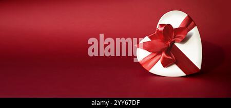 White paper box with ribbon isolated on red background, valentines day, copy space for text. Stock Photo