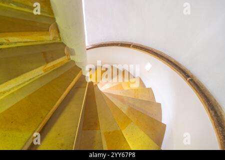 A beautifully designed spiral staircase descends gracefully, illuminated by soft sunlight streaming through an overhead window. The warm tones of the steps create a cozy atmosphere. Stock Photo