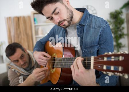 mature father with son sitting on sofa indoors playing guitar Stock Photo