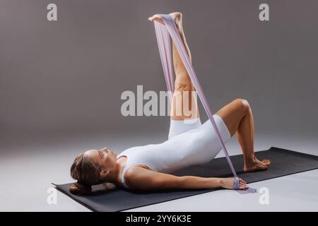 Athletic adult woman doing exercise with rubber band for fitness and pilates sitting on yoga mat.stretching exercises Stock Photo