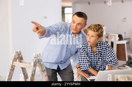 Man architect and boy using laptop while discussing working process in house being renovated Stock Photo