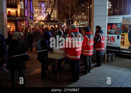 Hamburg, Germany. 19th Dec, 2024. Volunteer members of the German Red Cross (DRK) distribute food to homeless people on Gerhart-Hauptmann-Platz. A Christmas market can be seen in the background. Credit: Georg Wendt/dpa/Alamy Live News Stock Photo