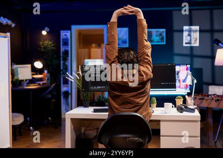 Developer doing software quality assurance, stretching after reading source code, feeling tired. IT admin relaxing muscles after inspecting coding to fix potential issues all day Stock Photo