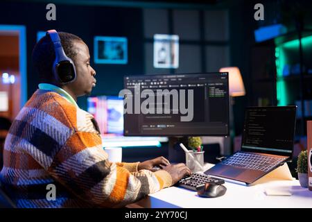 Black software engineer writes complex binary code scripts on computer, cybersecurity. Teleworking IT specialist in home office using programming language to safeguard consumer data. Stock Photo