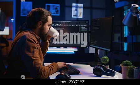 Stressed engineer feeling pressed by deadline, thinking how to finish developing code on PC. IT specialist brainstorming ways of solving database errors, working hard, drinking coffee, camera B Stock Photo