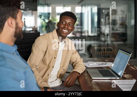 Happy African male employee having conversation with Latin colleague at work. Stock Photo