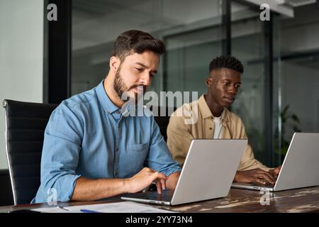Two busy diverse coworkers team using laptop working talking in office. Stock Photo