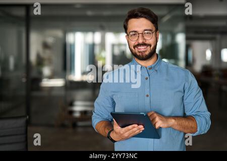 Happy young professional business man looking at camera at work using tablet. Stock Photo