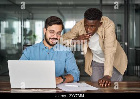 Two busy diverse professional coworkers discussing project working on laptop. Stock Photo