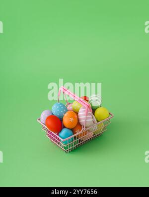 Easter composition made with colorful Easter eggs in pink shopping basket on pastel green background. Minimal Easter concept. Stock Photo
