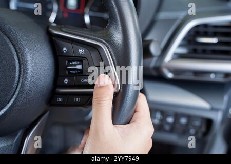 Woman's hand presses the button on the steering wheel of the car close-up. Multi function buttons on steering wheel in car. Back view of woman driver Stock Photo