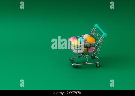 Easter composition made with colorful Easter eggs in  shopping cart on green background. Minimal Easter concept. Creative festive holiday layout. Stock Photo
