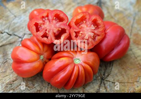 Close-up of whole and halved red ribbed tomatoes on an old tree stump as background. Concept of growing varietal tomatoes. Stock Photo