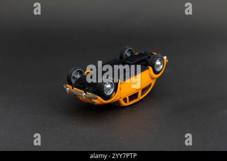 Yellow toy car over turn lying upside down on black background. Stock Photo