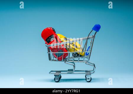 Toy cars inside mini shopping cart on blue background Stock Photo