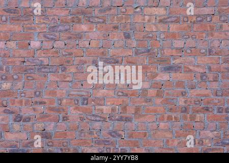 A detailed image of a textured red brick wall, showcasing varied shades of red and brown with rough, weathered surfaces. Stock Photo
