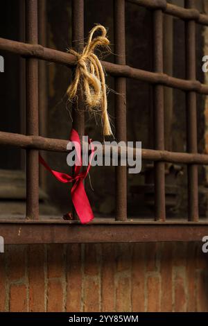 A red ribbon and a piece of rope tied to rusty bars Stock Photo