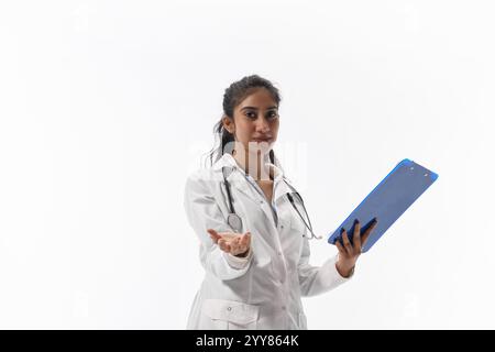Young attractive Indian woman, dressed medical uniform and reaching hand to camera, showing support and care against white studio background. Stock Photo
