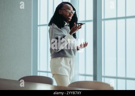 A black entrepreneur using a smartphone for a conference call in a contemporary office. The female professional is focused and confident, engaged in r Stock Photo