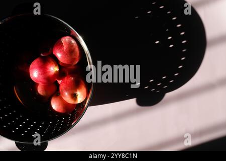 Red Apples in Colander and Dramatic Shadows on Lilac Backdrop Stock Photo